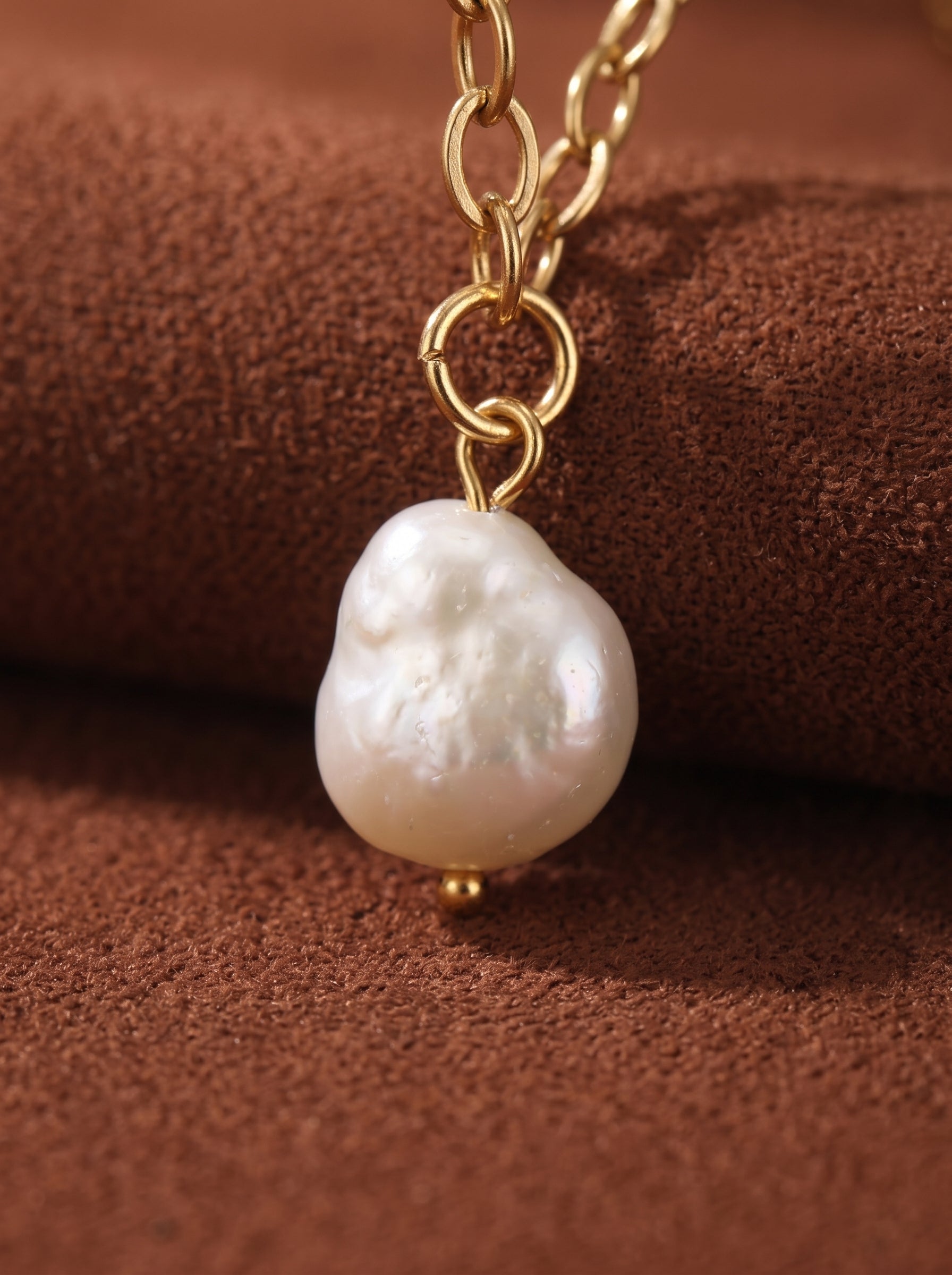 Gros plan d'un collier à chaîne dorée présentant une lustrée perle baroque blanche d'eau douce avec un petit accent en perle dorée. @pearl