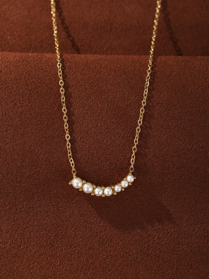 Arcadia - Freshwater Pearl Curved Bar Necklace featuring a delicate gold chain and a gracefully curved bar adorned with seven luminous white freshwater pearls of varying sizes.