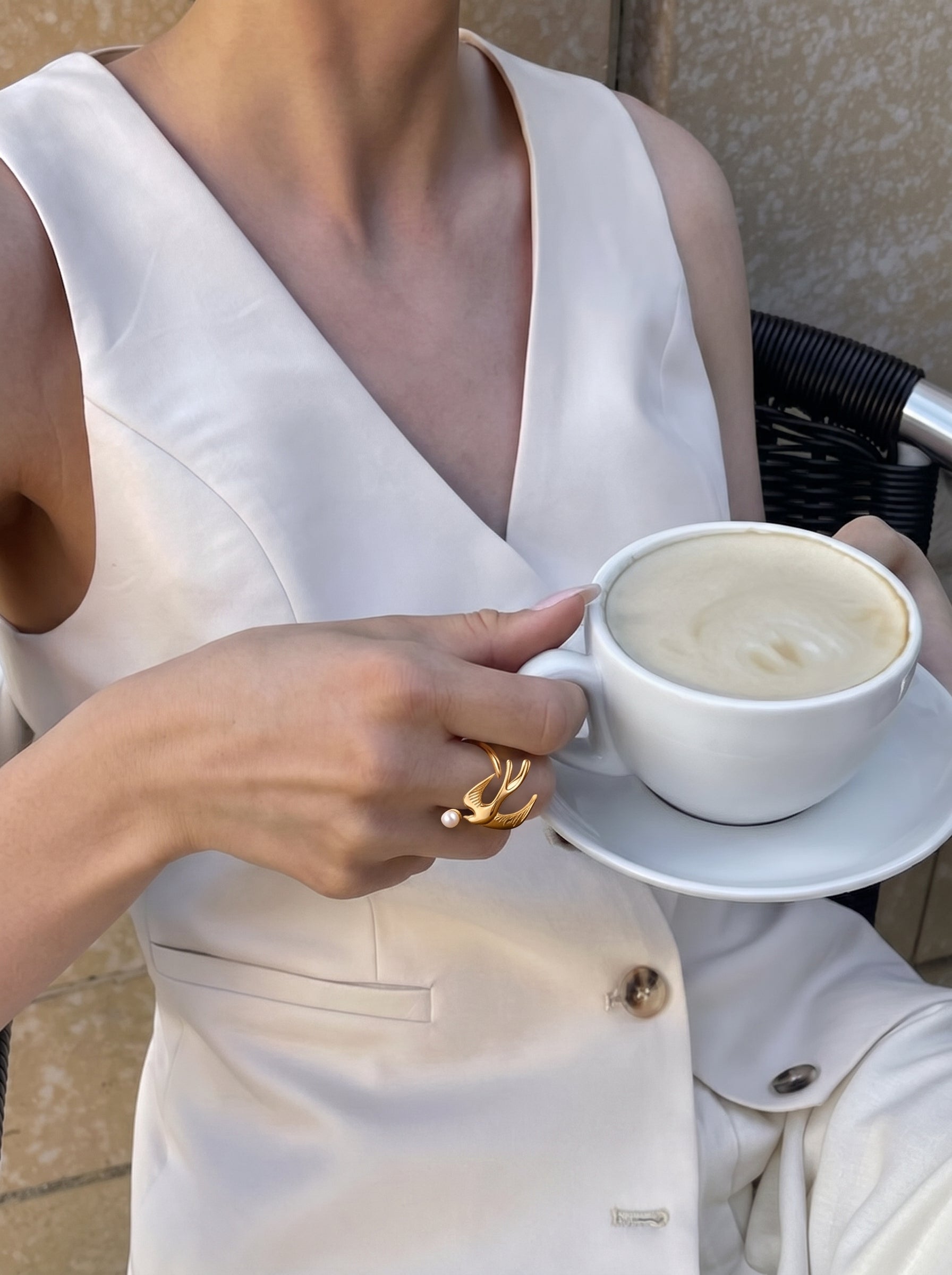Une femme portant une bague manchette oiseau dorée Ascending en perle d'eau douce au doigt tout en tenant une tasse de café. @lifestyle