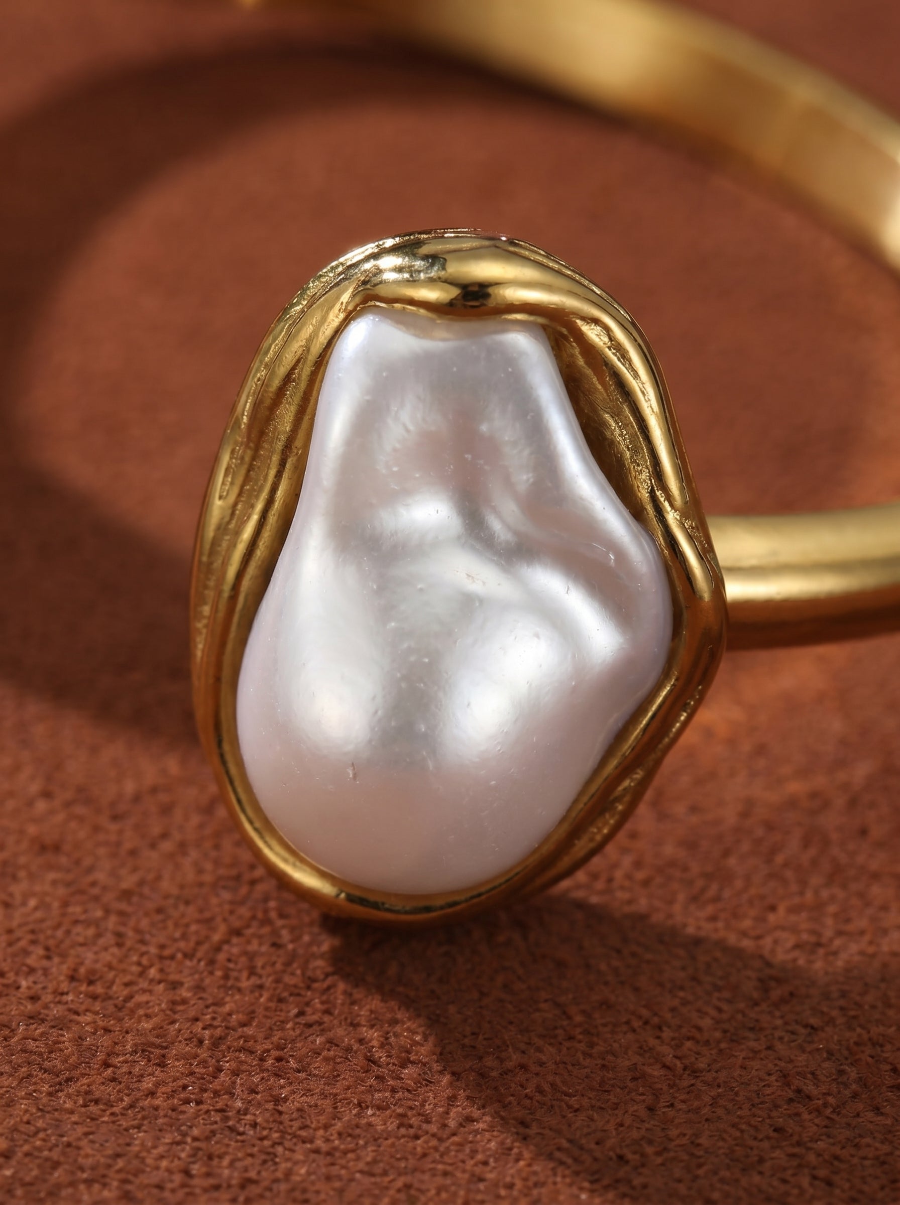 Close-up of a gold cuff bracelet showcasing a large, irregular white freshwater Baroque pearl with a textured setting.@pearl