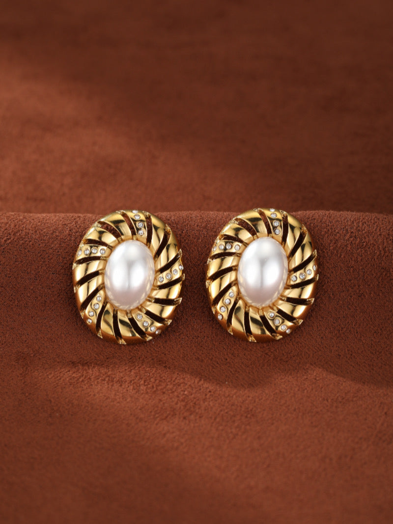 Aurelian gold-toned stud earrings featuring a central oval freshwater pearl surrounded by a sculptural spiral design with sparkling accents.