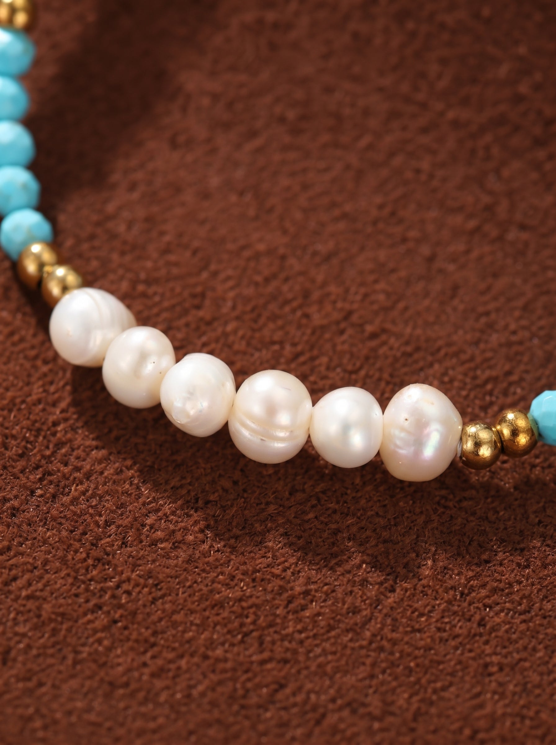 Close-up of the Azure Drift necklace, featuring a strand of luminous white freshwater pearls interspersed with small gold beads and turquoise-colored beads, presented on a textured brown background. @pearl