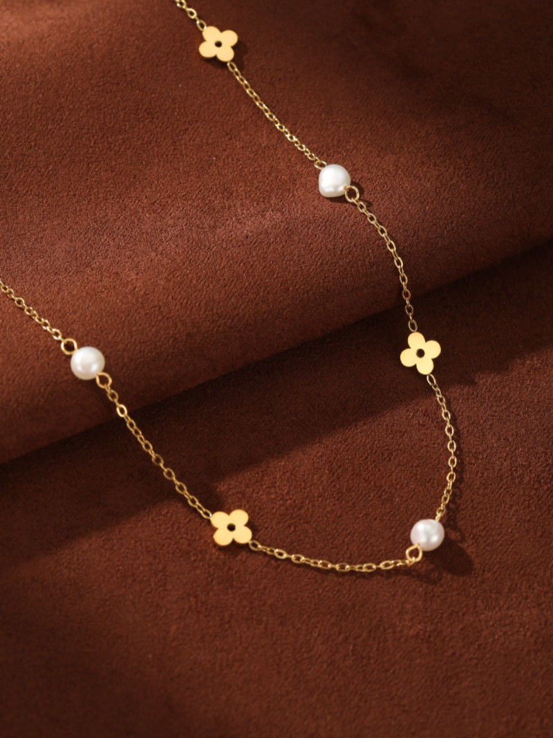 Gold-tone chain necklace with small flower charms and 4mm freshwater button pearls, displayed on a brown textured background. @pearl