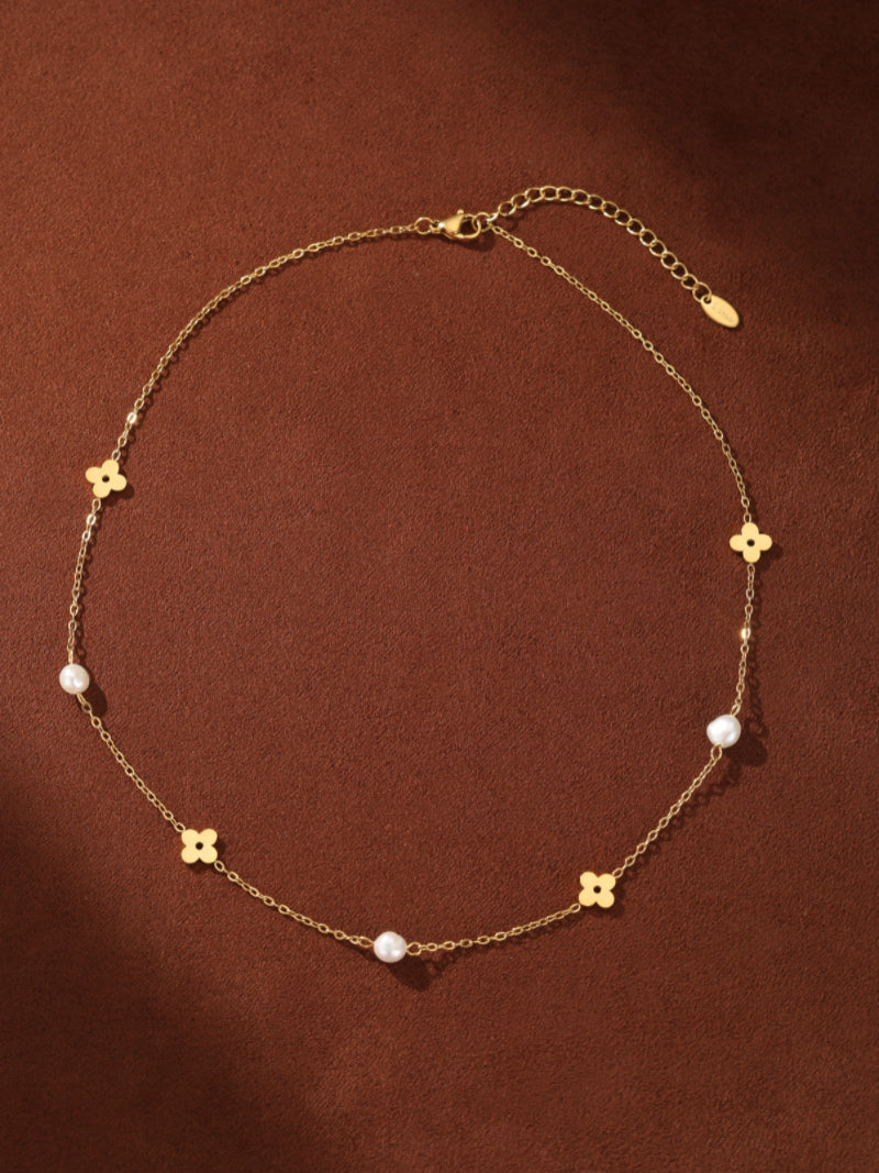 Gold-tone chain necklace with alternating clover flower charms and 4mm button freshwater pearls, displayed on a brown background. @pearl