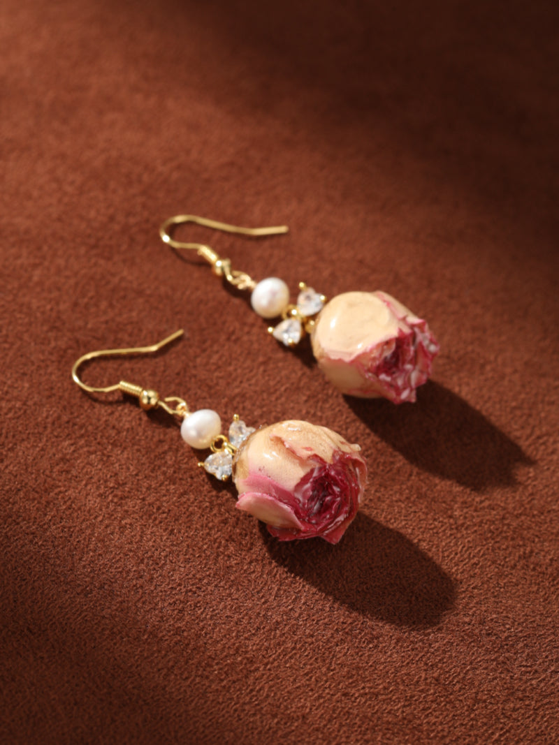 Botanical Dew Freshwater Pearl Flower Dangle Earrings featuring a real dried rosebud with pink and cream petals, a lustrous white pearl, and a sparkling bow accent, dangling from gold hooks. @pearl