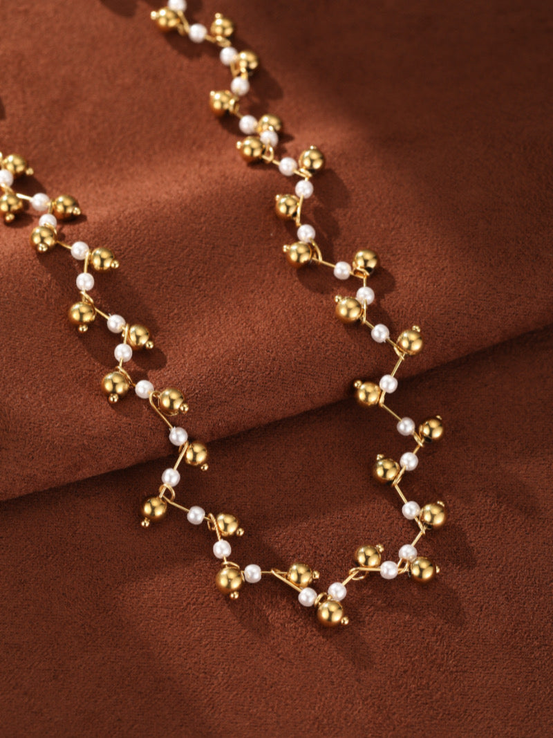 Branch Weave Mother of Pearl Twist Beaded Necklace with small white pearls and gold beads on a brown textured background.