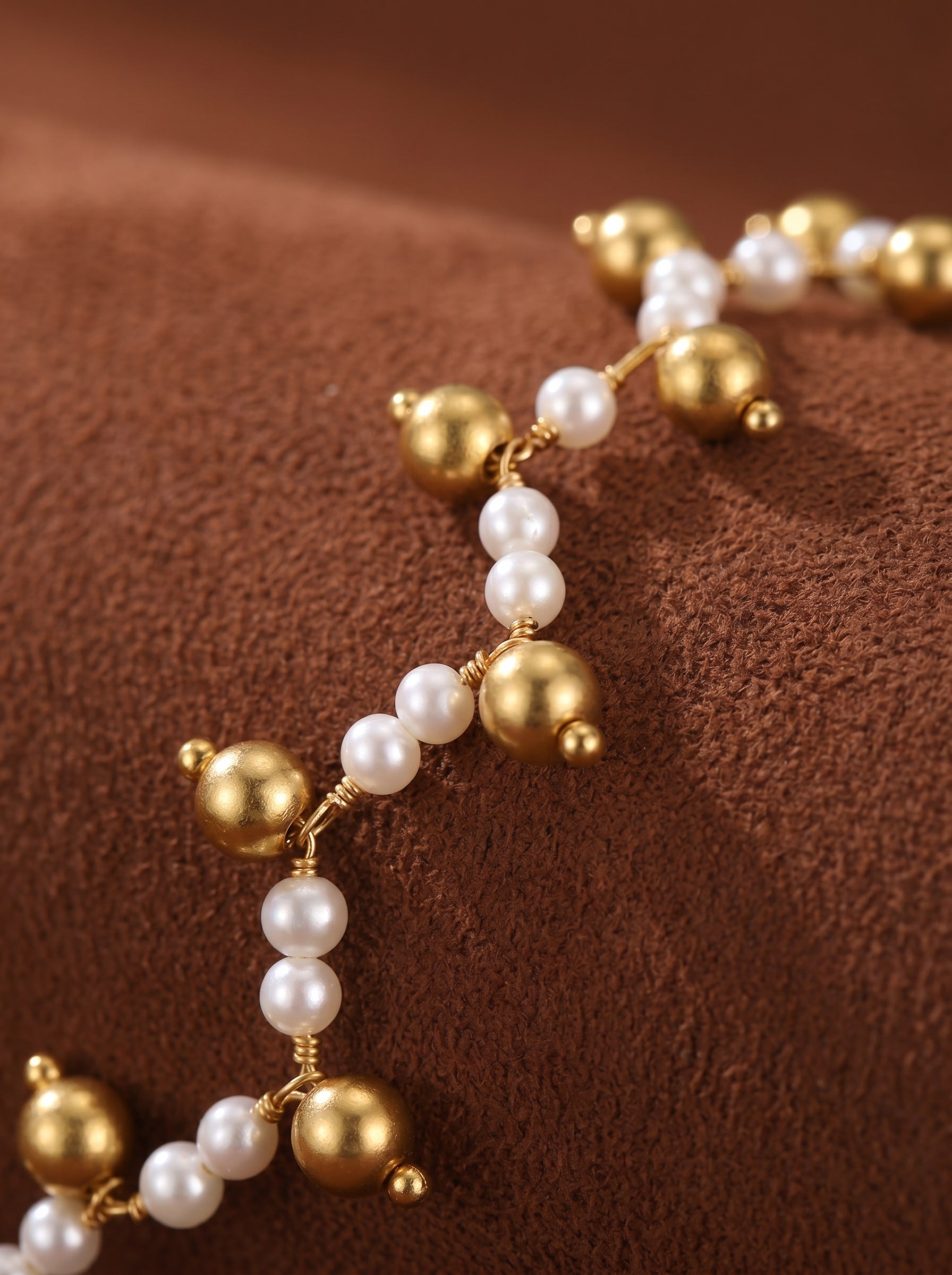 Close-up of the Branch Weave Mother of Pearl Twist Beaded Necklace, featuring small white pearls and gold-toned beads intertwined with delicate gold wire on a brown textured background. @pearl