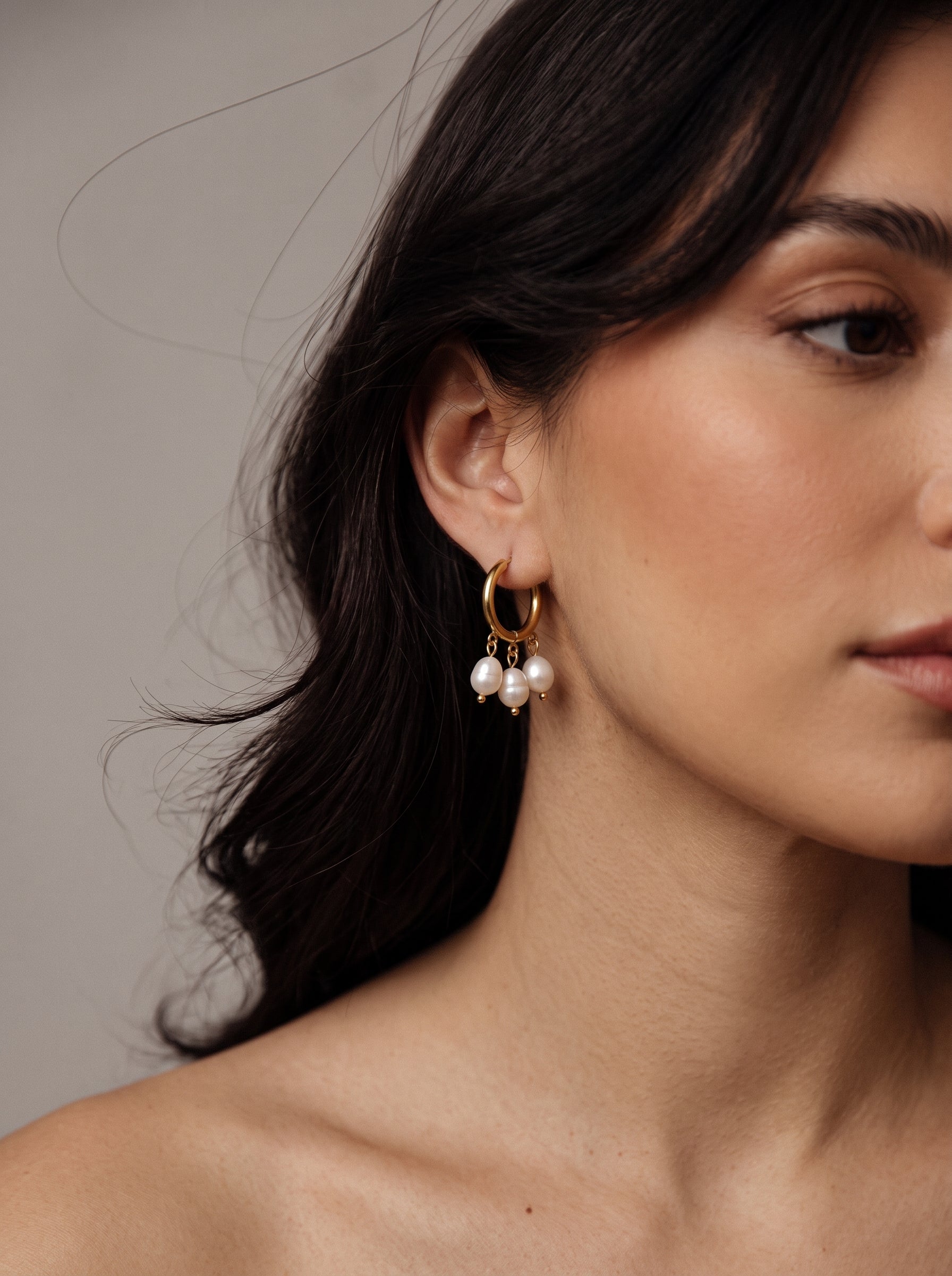 Gros plan d'une femme portant des créoles ton or avec trois perles blanches pendantes d'eau douce. @model