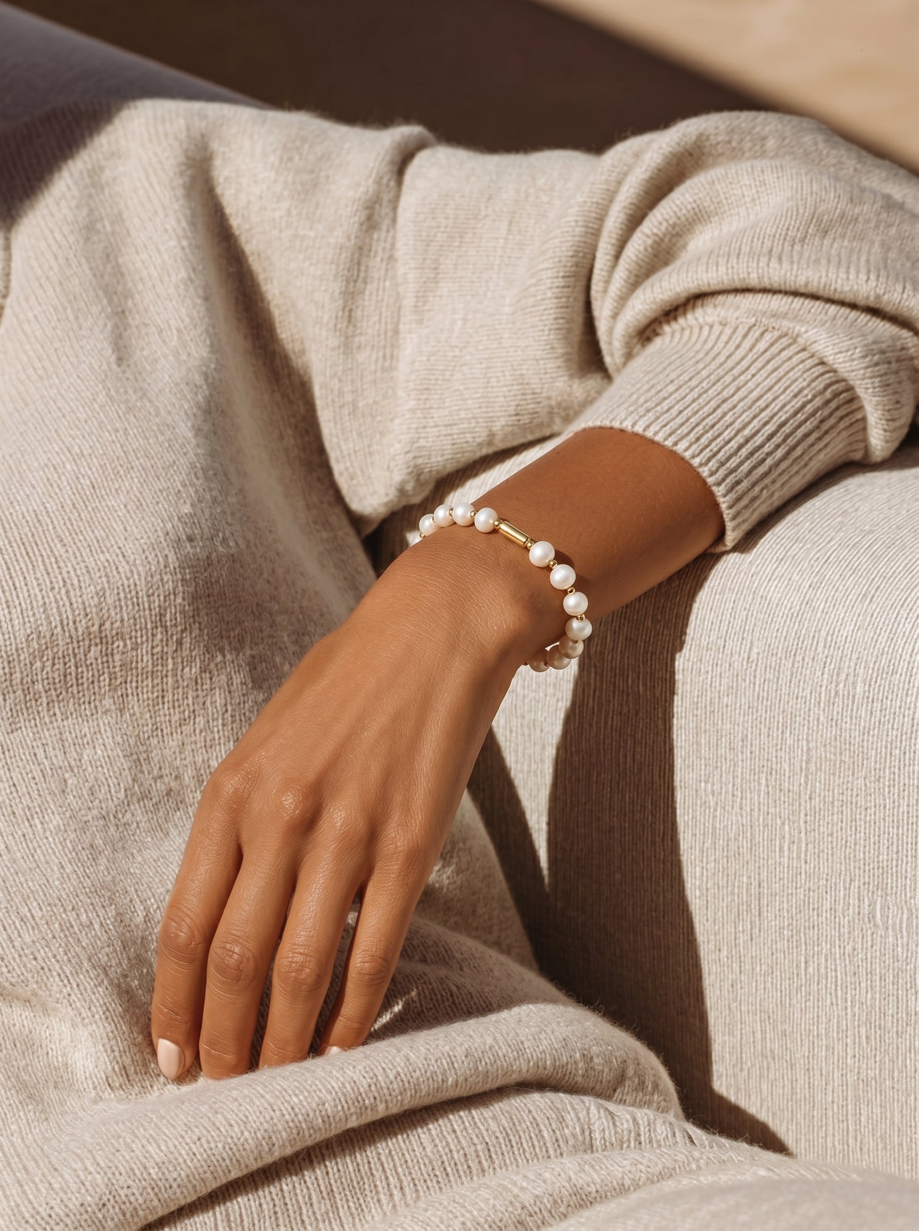 A woman's arm wearing the Cadence Freshwater Pearl Beaded Bracelet, featuring luminous white seed pearls and gold-toned accents, layered with a neutral-toned sweater. @lifestyle