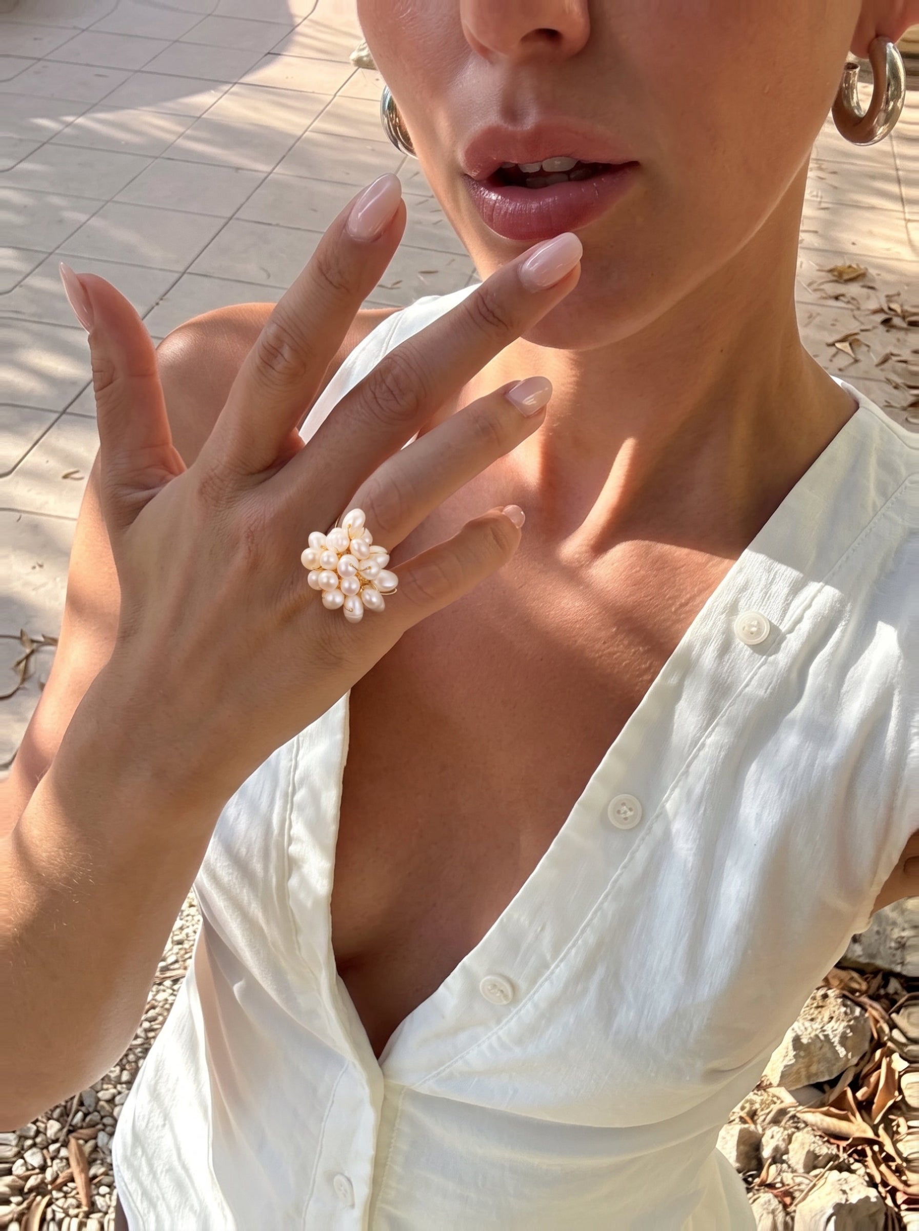 A woman's hand wearing the Caprice Freshwater Pearl Beaded Ring, showcasing the cluster of 3mm white baroque pearls arranged in a modern beaded design. The image is a lifestyle shot with dappled sunlight and an outdoor setting. @lifestyle