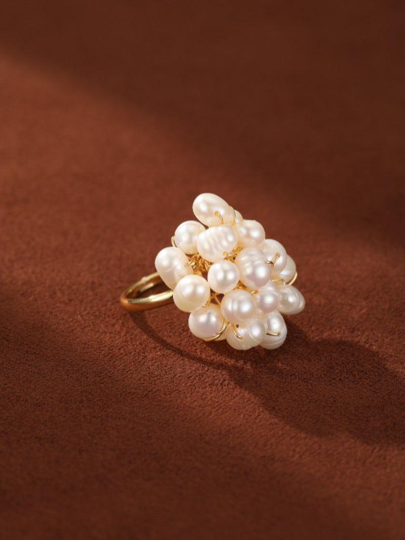 Caprice Freshwater Pearl Beaded Ring featuring a cluster of irregular white baroque pearls on a gold-tone band against a brown background.
