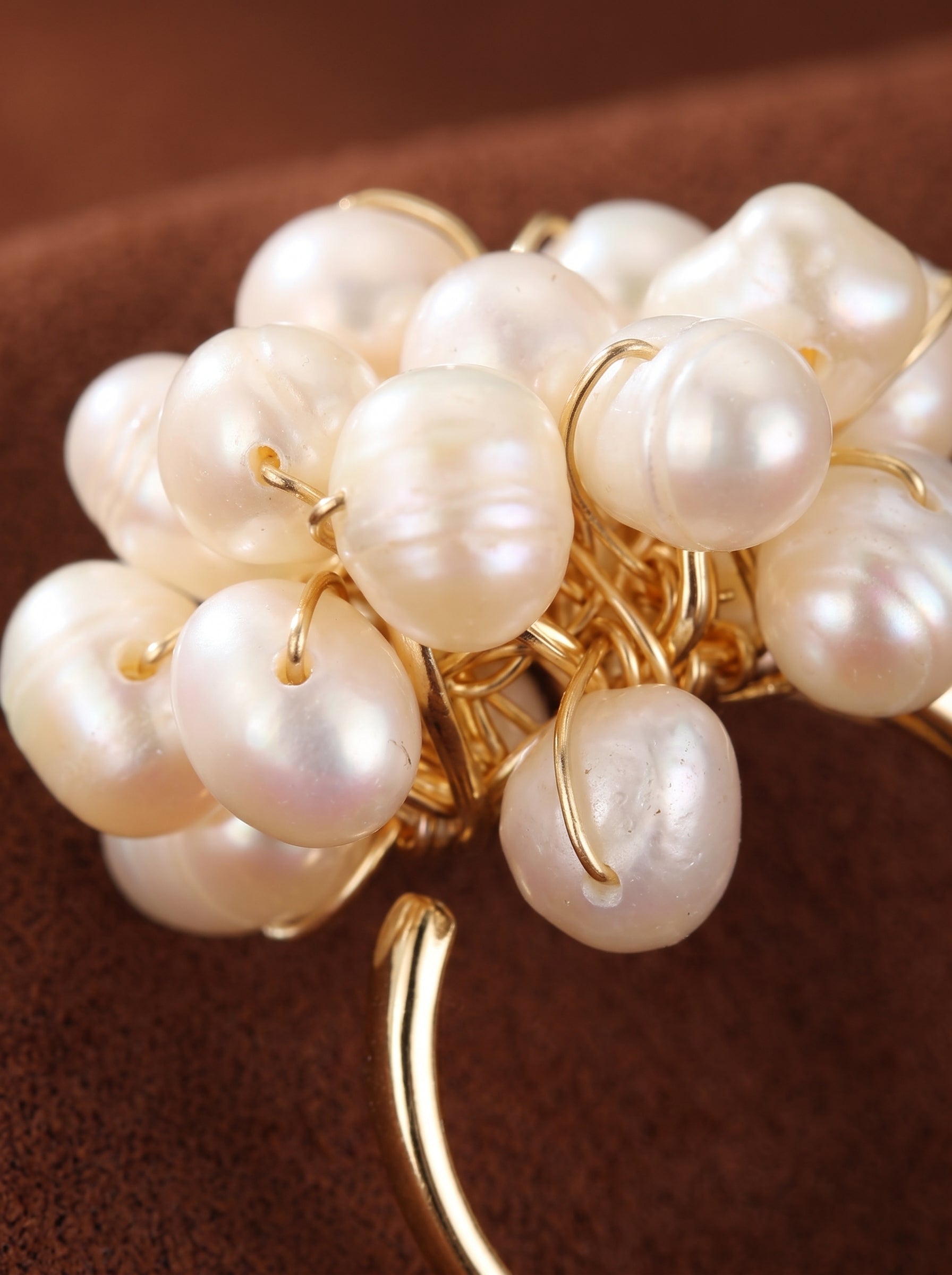 Close-up of the Caprice ring featuring a cluster of irregular white freshwater pearls beaded onto a gold band, set against a brown textured background. @pearl