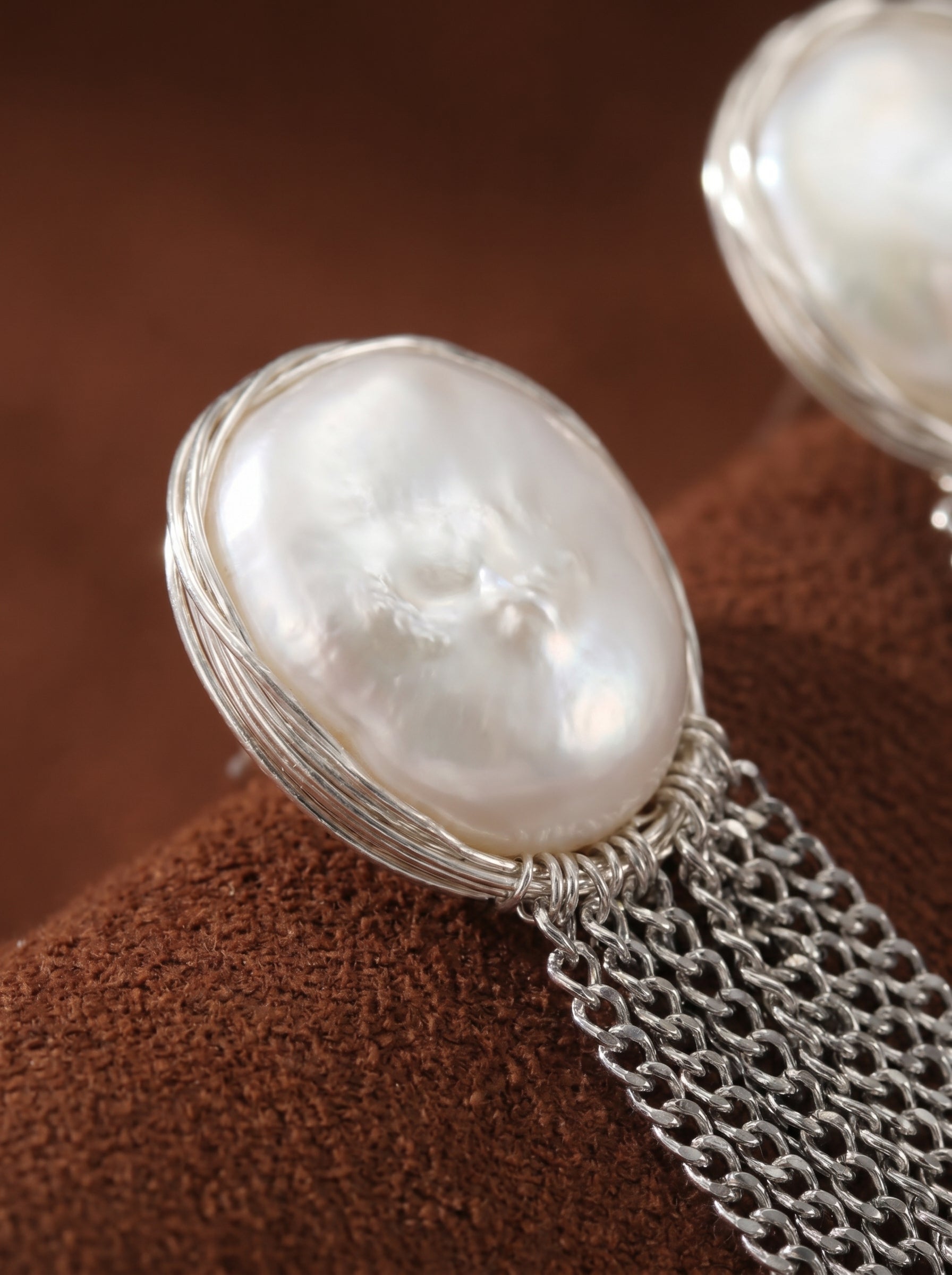 Close-up of Cascade freshwater pearl fringe dangle earrings featuring a large, irregular white baroque pearl wrapped in silver wire with a silver chain fringe dangling below. @pearl
