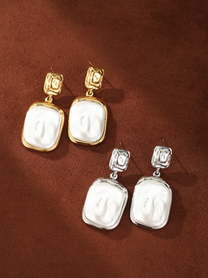 Une paire de boucles d'oreilles pendantes ton or et une paire ton argent, chacune présentant une puce carrée martelée suspendant un relief en perle baroque blanche d'eau douce aux textures organiques.