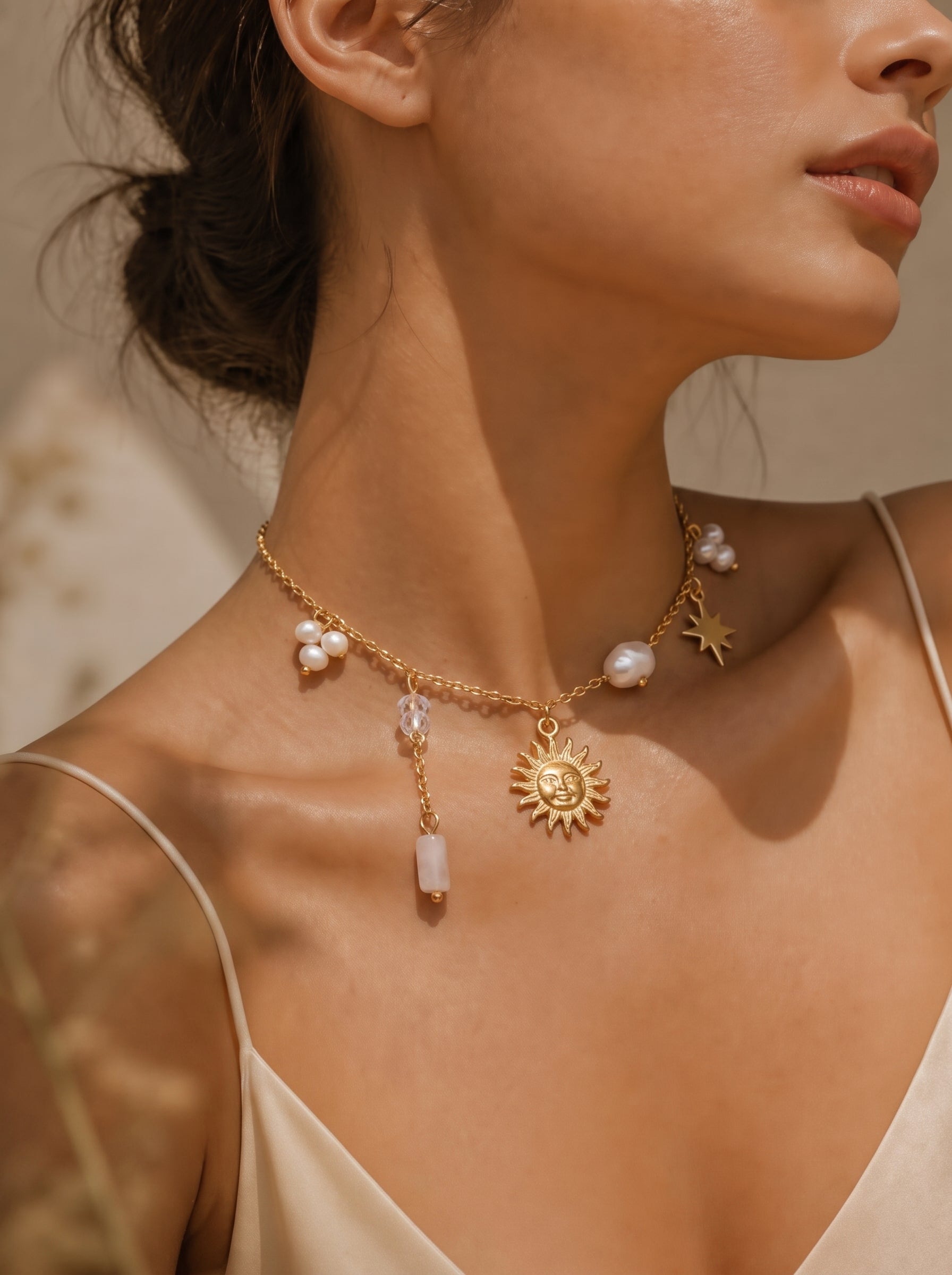 A gold-toned necklace with a sun pendant, star charm, and floating freshwater pearls is worn by a model. @model