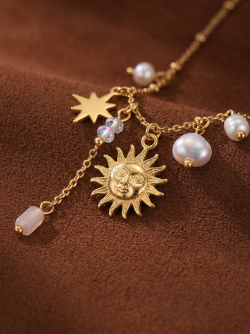 Close-up of a celestial-themed gold necklace featuring a sun pendant, a star charm, and several floating freshwater pearls on a textured brown background.