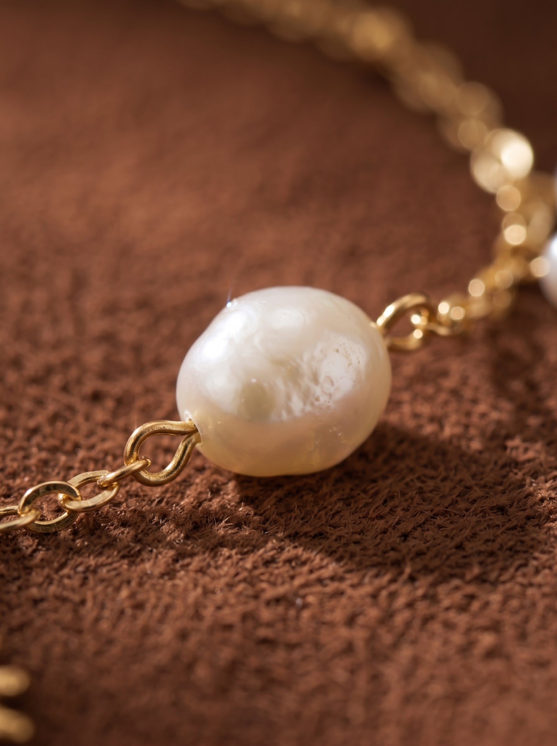 Gros plan d'un collier à chaîne dorée présentant une seule perle baroque flottante d'eau douce et une touche de breloque soleil. @pearl
