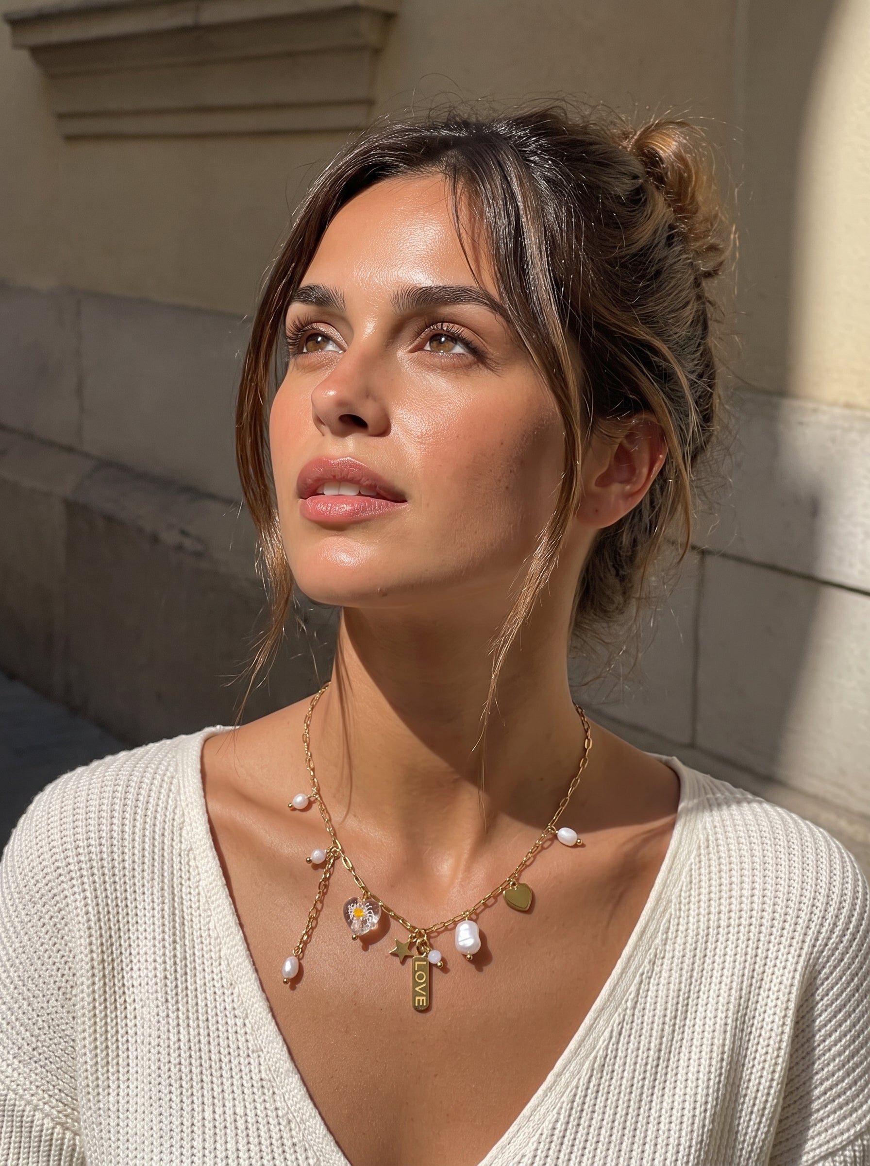 Gros plan d'une femme portant le collier ton or Celestial Whim avec des perles baroques flottantes d'eau douce, une breloque étoile, une breloque cœur, et une étiquette « LOVE ». @lifestyle