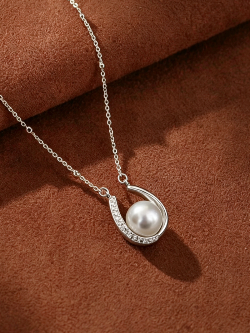 Silver-toned chain necklace featuring a horseshoe pendant cradling a luminous Akoya pearl, with pavé-set accent stones on one side of the horseshoe.