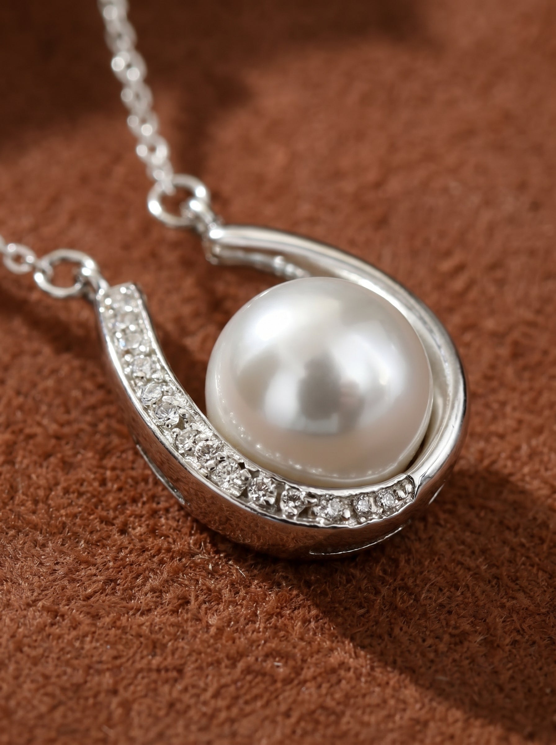Silver-toned chain necklace featuring a horseshoe pendant adorned with pavé accent stones, cradling a luminous 8mm Akoya pearl. The pearl has a lustrous, round, silver hue.