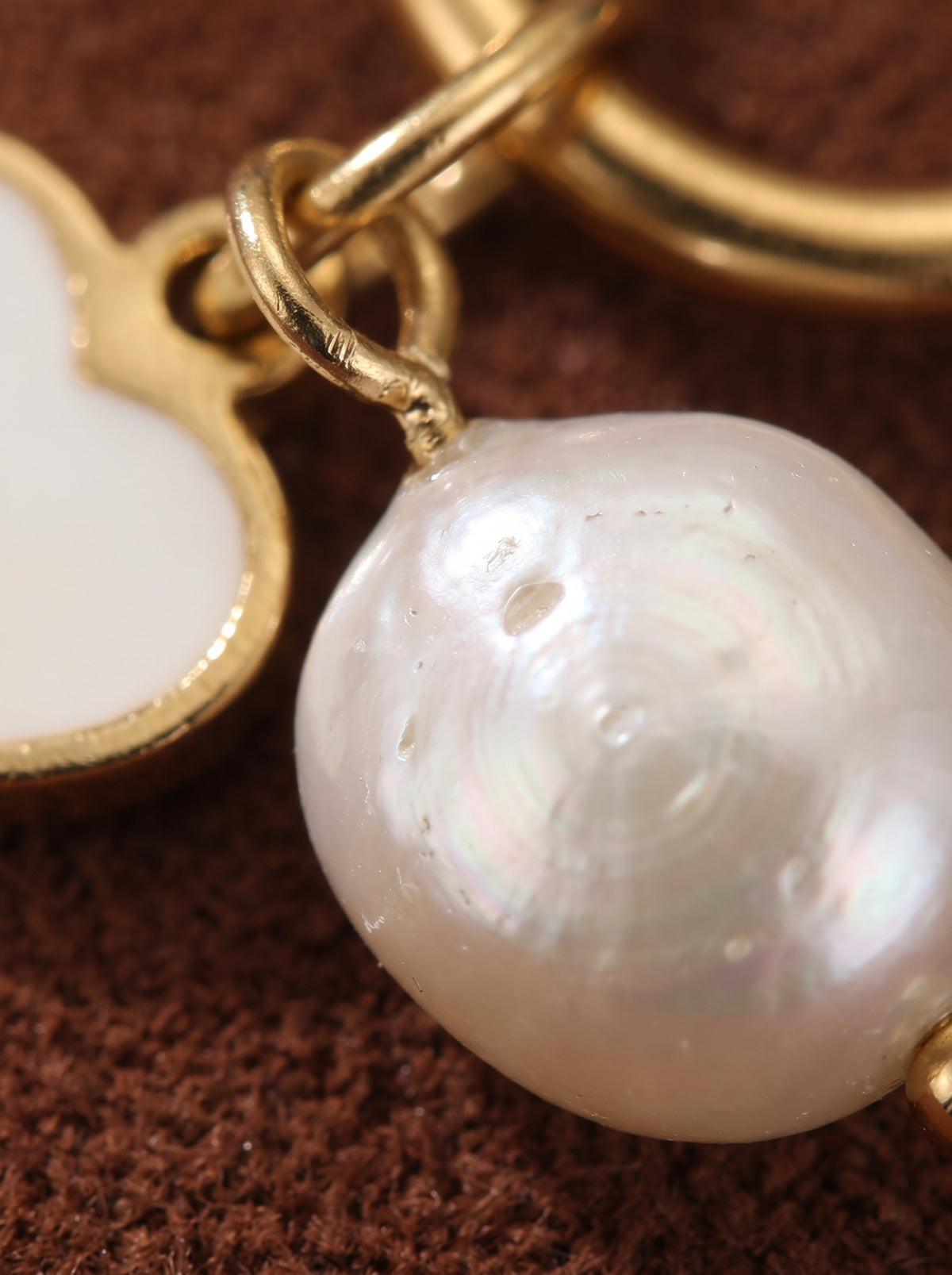 Gros plan des boucles d'oreilles créoles pendantes cœur Cherish en perle d'eau douce, révélant une lumineuse perle baroque blanche et une breloque cœur dorée. @pearl