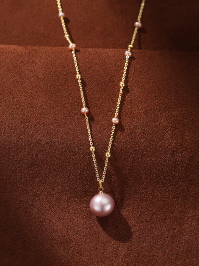A delicate gold-tone chain necklace featuring a large, lustrous pink freshwater pearl pendant and smaller pink pearls interspersed along the chain, creating a floating effect.