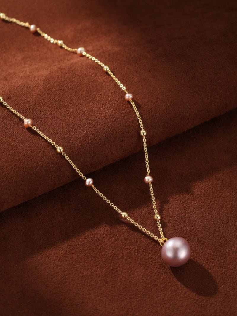 Delicate gold-tone chain necklace featuring a large pink freshwater pearl pendant and smaller interspersed pink pearls and gold beads, creating a floating effect.