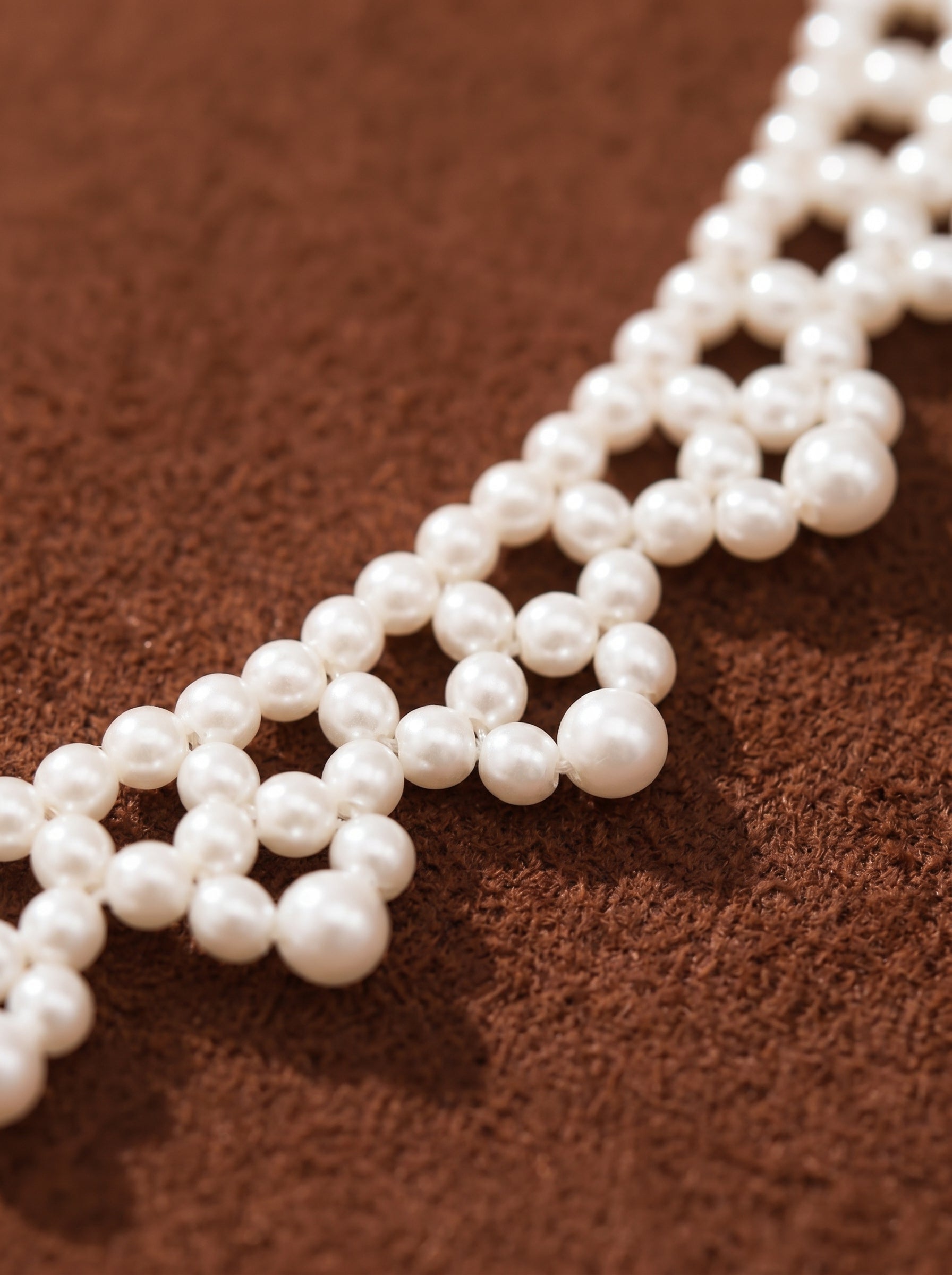 Close-up of the Cipher Freshwater Pearl Woven Choker Necklace, featuring small and medium white freshwater pearls in a delicate lattice pattern on a brown textured background. Freshwater Pearl Woven Choker Necklace@pearl