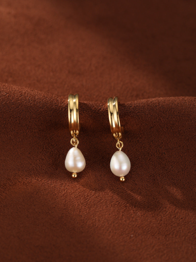 Gold hoop earrings featuring a drop of a lustrous 8mm white freshwater pearl on a brown background.