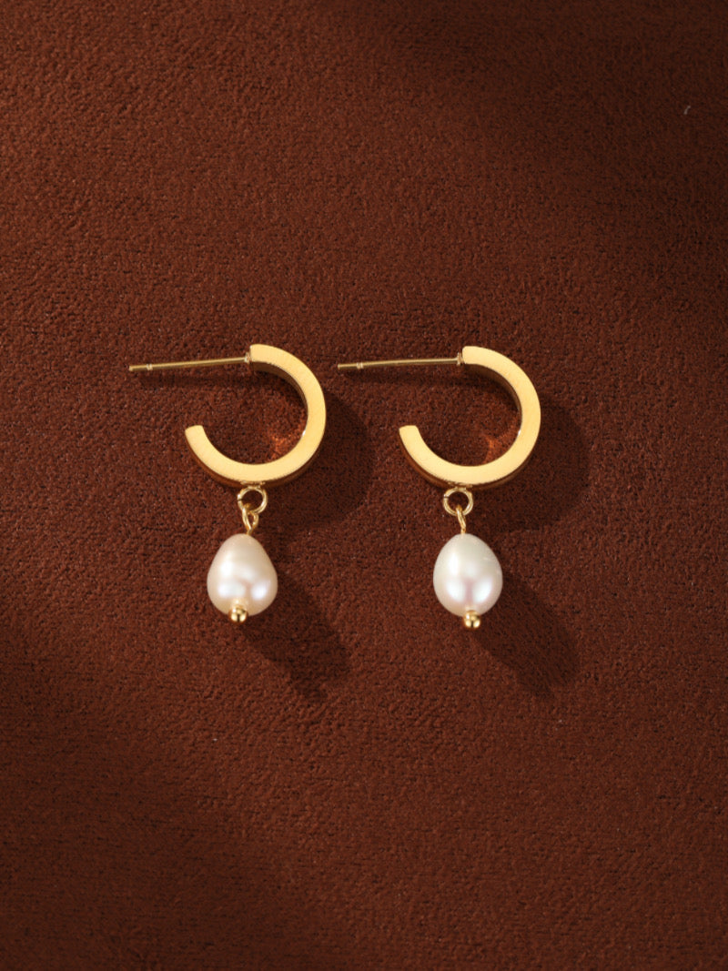 A pair of gold-toned hoop earrings with white freshwater pearl drops, displayed on a brown background.