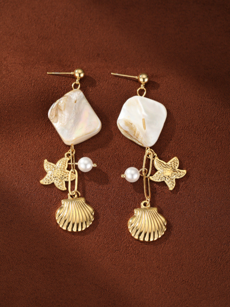 Boucles d'oreilles pendantes ton or Coastal Allure présentant des perles blanches d'eau douce, des carrés en nacre, des étoiles de mer dorées, et des breloques coquillage dorées.