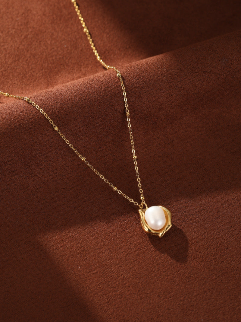 Collier à chaîne perlée ton or présentant une perle blanche d'eau douce sertie dans un pendentif vase sculptural ton or.