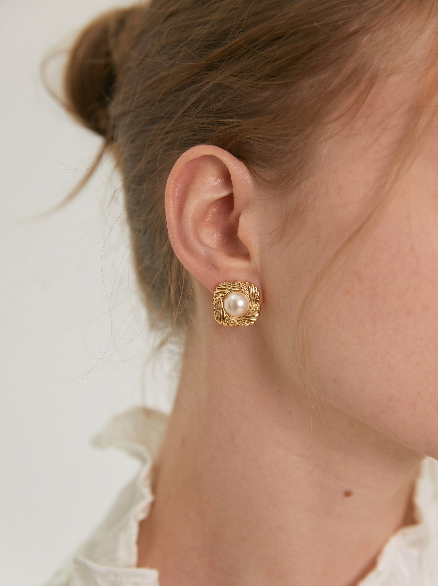 Gros plan de l'oreille d'une femme portant les boucles d'oreilles puces carrées Coffer ton or avec un cadre texturé et une lumineuse perle baroque blanche d'eau douce de 8 mm ou 10 mm au centre. @model