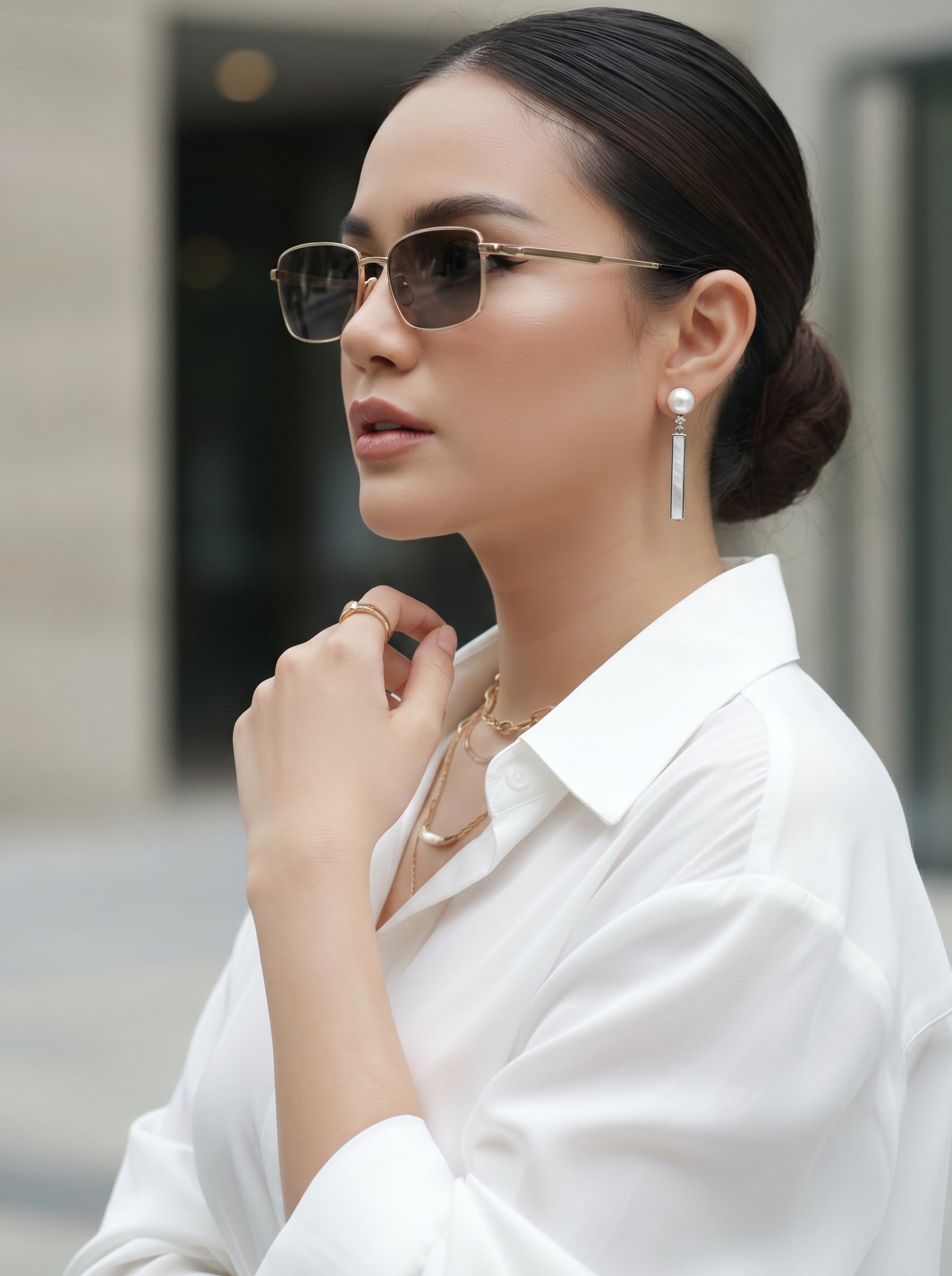 A woman wearing a white collared shirt and sunglasses, accessorized with pearl stud drop earrings and layered gold necklaces. @lifestyle #lifestyle