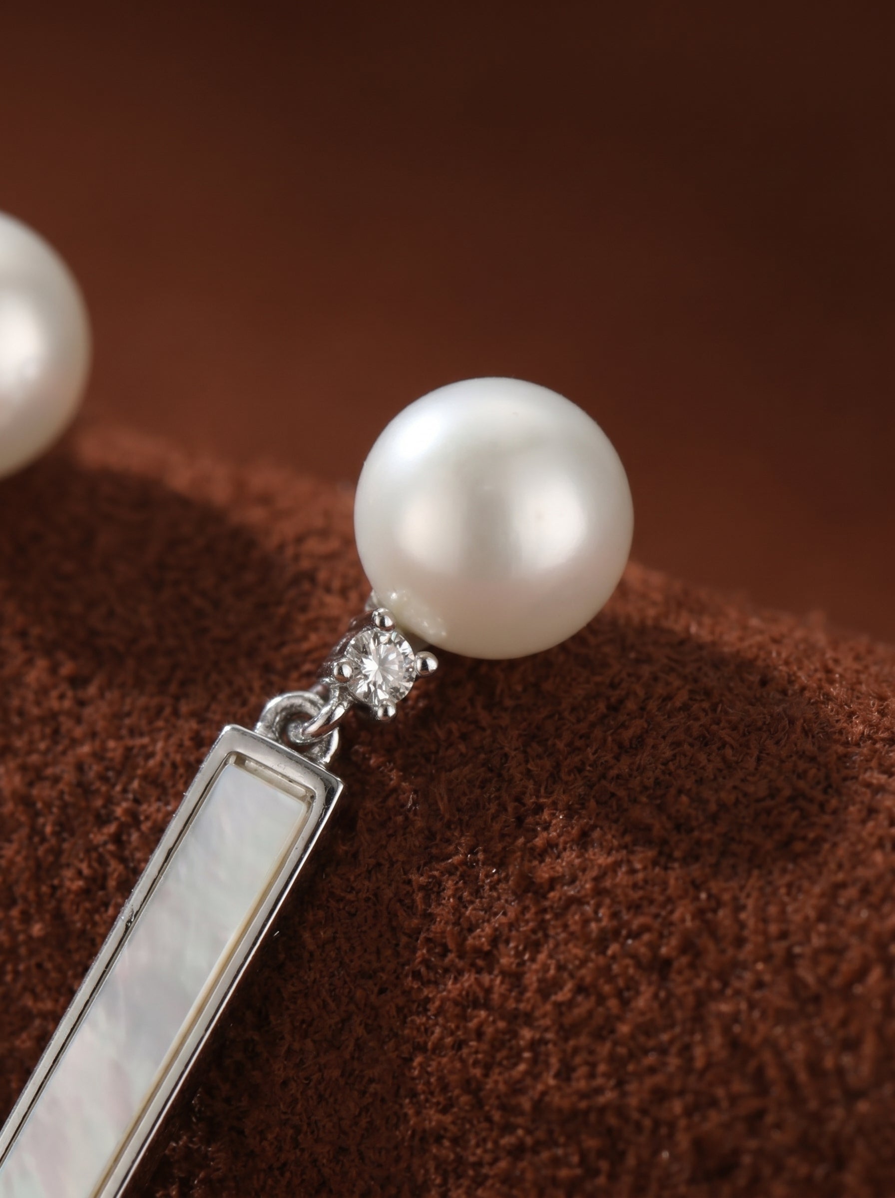 Close-up of a delicate drop earring featuring a lustrous white freshwater pearl stud, a small sparkling accent gem, and a rectangular drop with mother-of-pearl inlay. @pearl