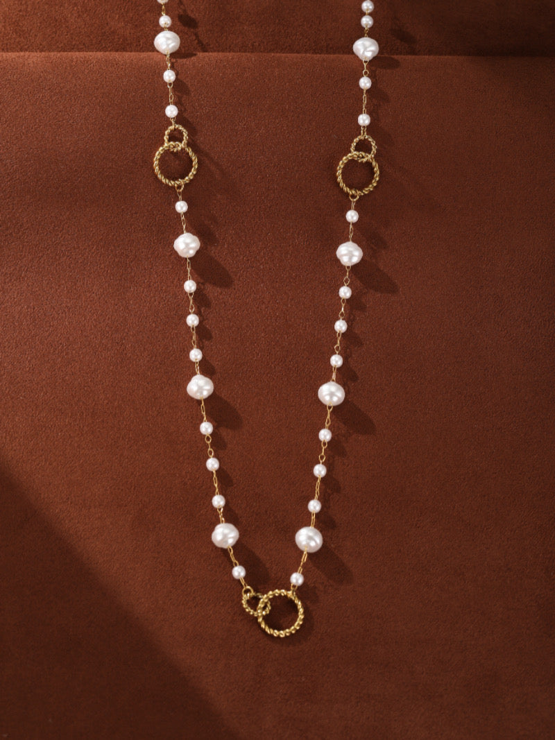 A long, gold-tone necklace with a delicate chain, interspersed with varying sizes of white imitation baroque pearls and textured gold-tone rings.