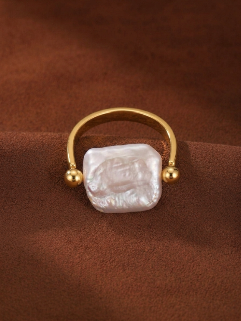 Gold-toned cuff ring with a large, irregular white freshwater pearl on a brown textured background.