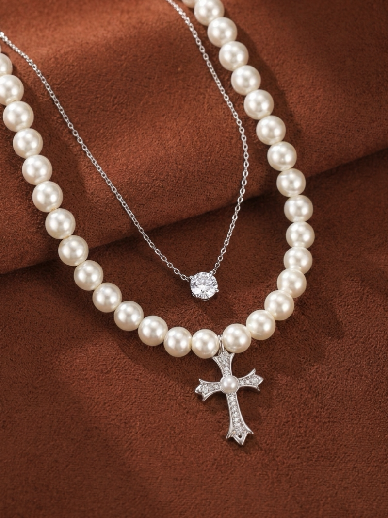 Layered necklace featuring a strand of white imitation pearls with an embellished cross pendant and a delicate silver chain with a solitaire crystal pendant.