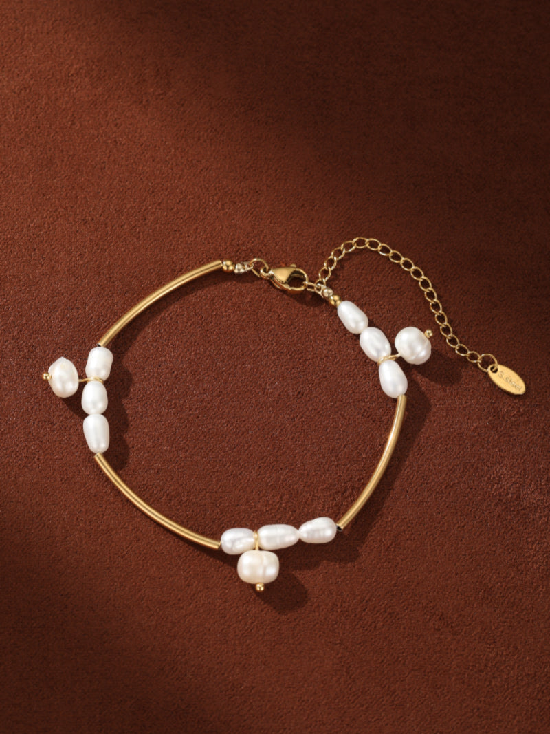 Gold-toned chain bracelet featuring irregular white freshwater seed pearls set on a curved bar with an adjustable extender chain, displayed on a textured brown background. @pearl