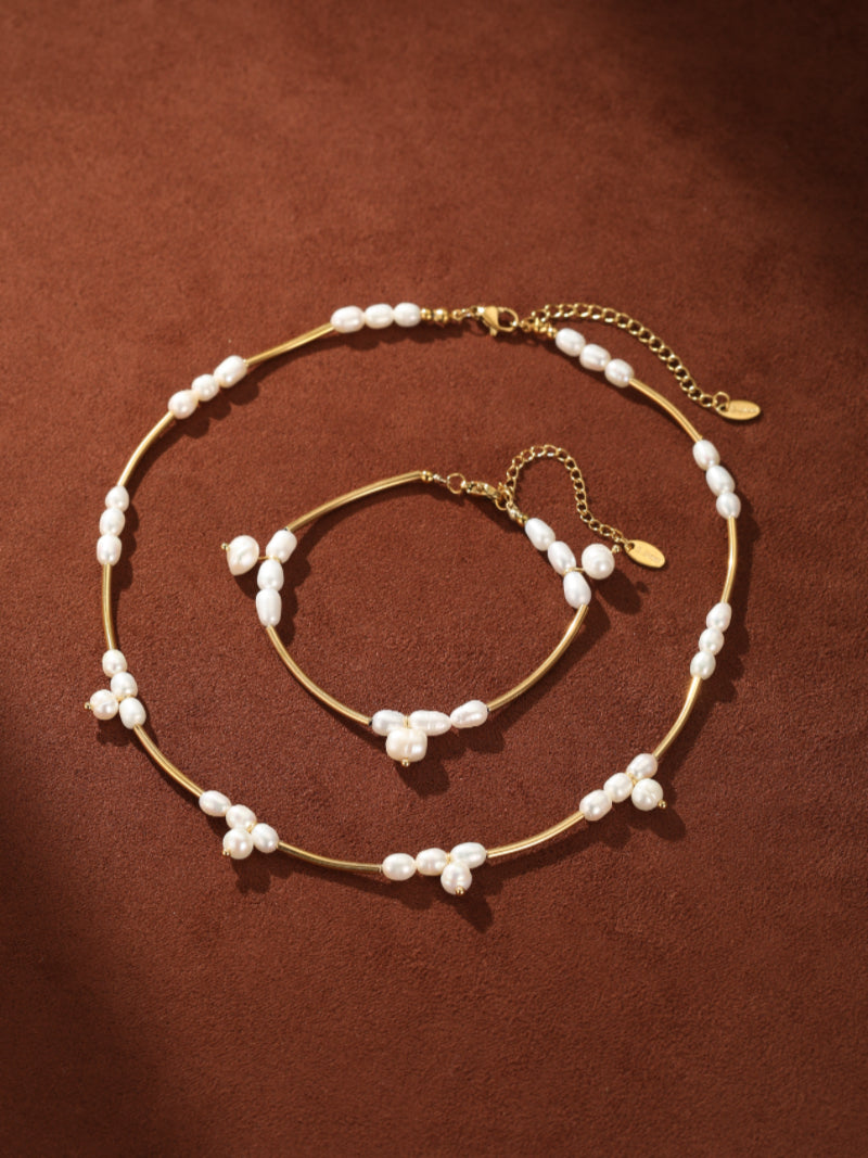 Gold-toned chain bracelet and necklace set featuring irregular white freshwater seed pearls spaced along the chains and clustered at intervals, displayed on a textured brown background. @pearl