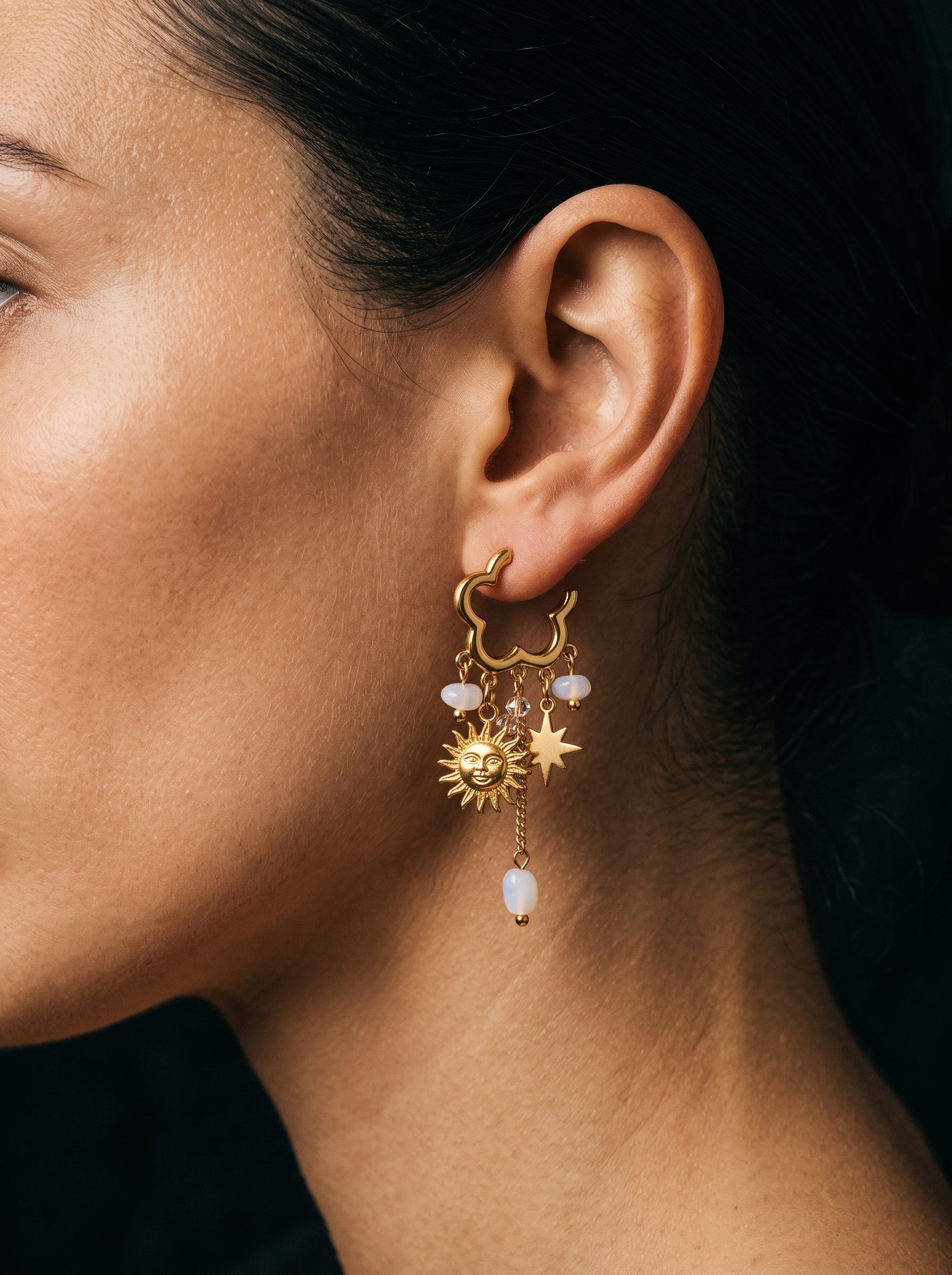 Close-up of a model wearing gold dangle earrings featuring freshwater pearls, a sun charm, and a star charm. @model