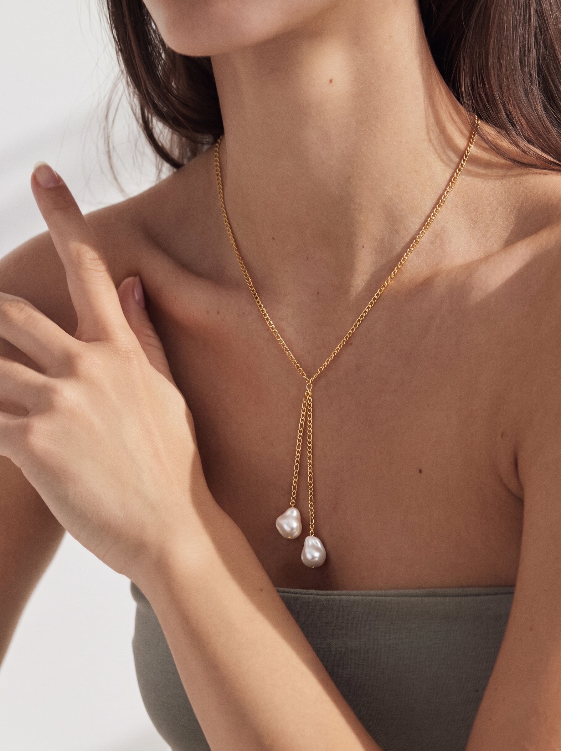 A woman wears a gold-toned lariat necklace featuring two irregular white imitation pearls, showcasing the pendant design on her décolletage. @model