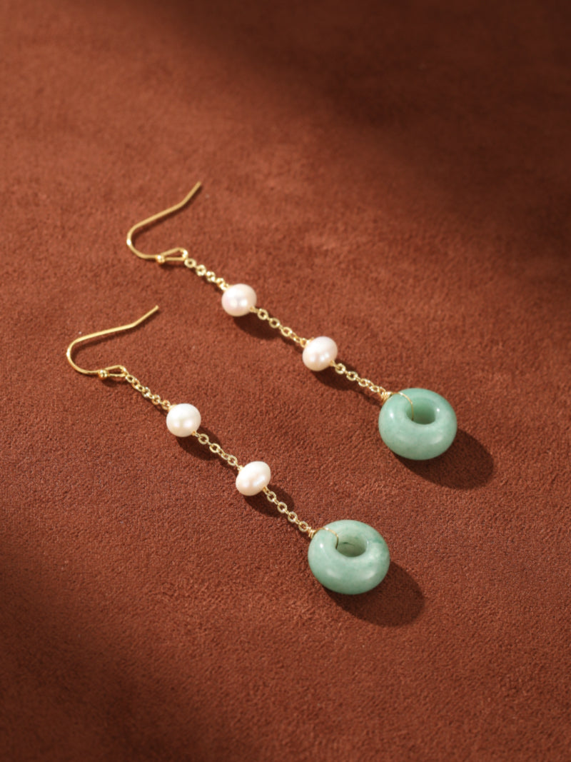Dewdrop Freshwater Pearl Ring Dangle Earrings featuring white seed pearls and green jade rings on a delicate gold chain, displayed against a brown textured background. @pearl
