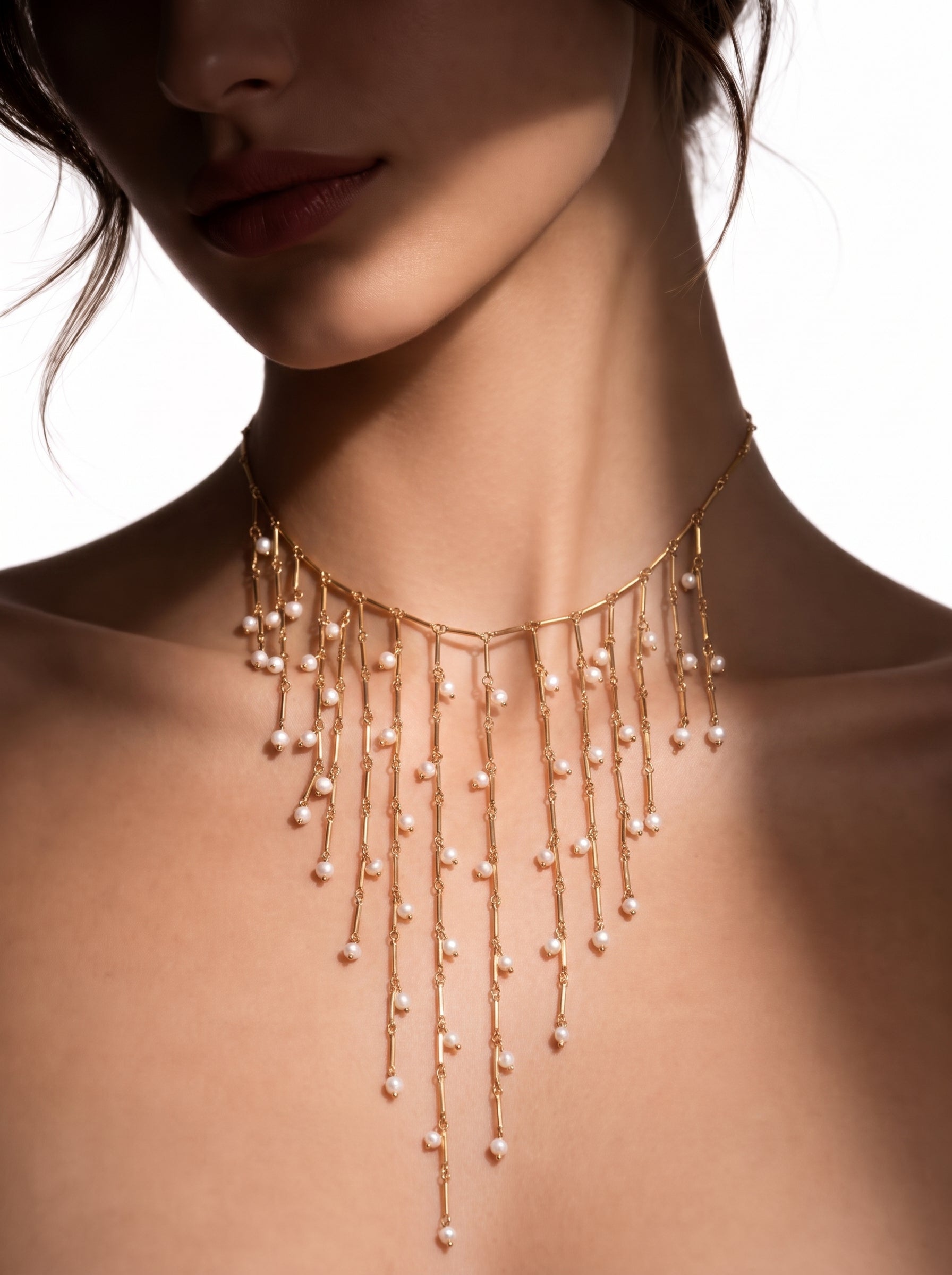 Un long collier doré à plusieurs rangs de fines barres ornées de lumineuses perles graines d'eau douce, cascadant sur le décolleté d'une mannequin. @model
