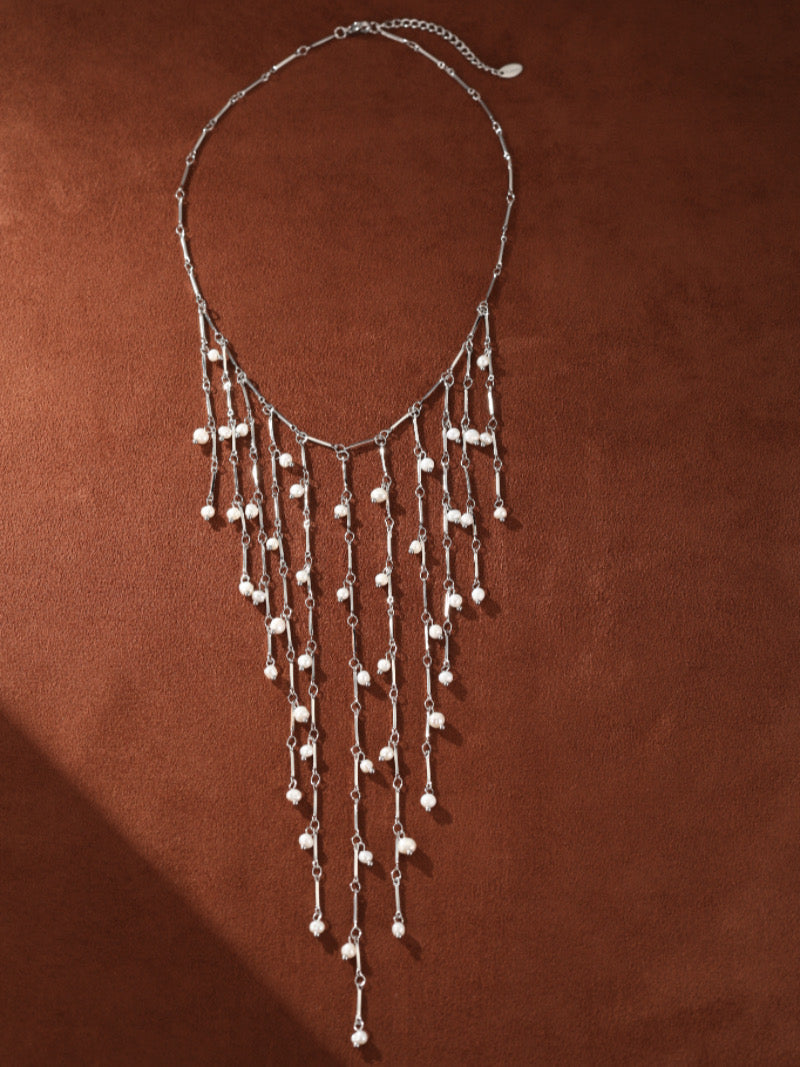Long collier Dewfall au design cascade, présentant de multiples rangs argentés délicats ornés de lumineuses perles graines d'eau douce de 3 mm. Le collier a une silhouette moderne et est présenté contre un fond marron.