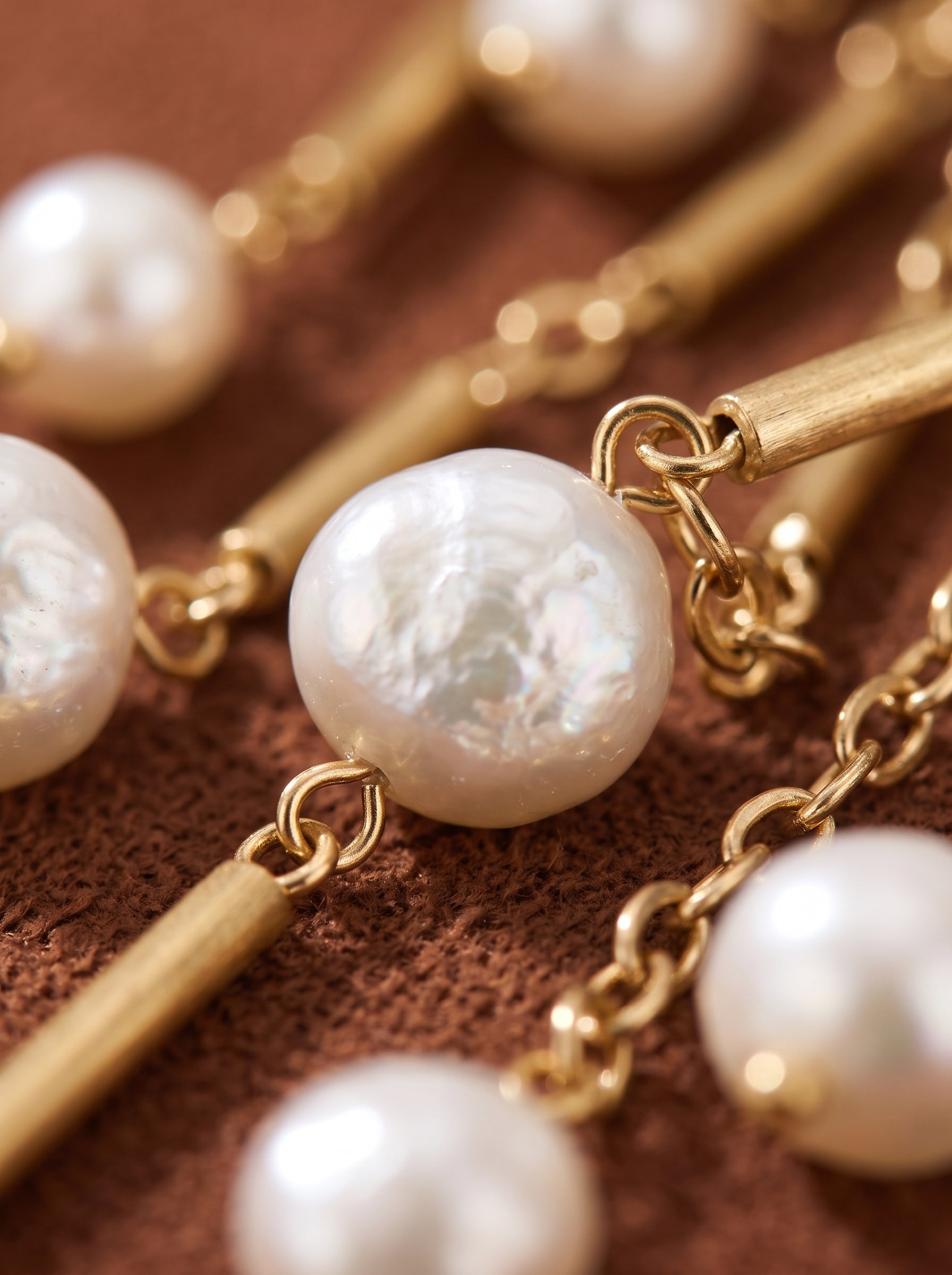 Gros plan du long collier Dewfall en perle d'eau douce, présentant de lumineuses perles graines blanches et des barres mates dorées sur une délicate chaîne dorée. @pearl