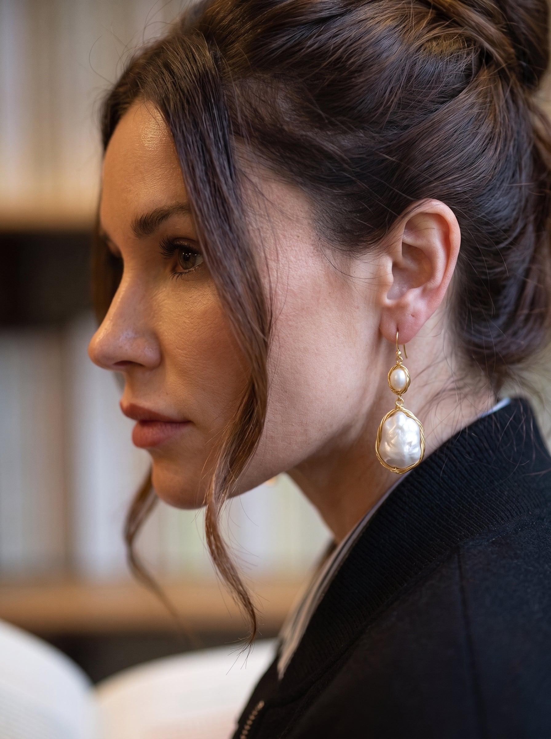 Close-up of a woman wearing Drift freshwater pearl wire-wrapped dangle earrings while reading a book in a library, bookshelves in the background @lifestyle #lifestyle