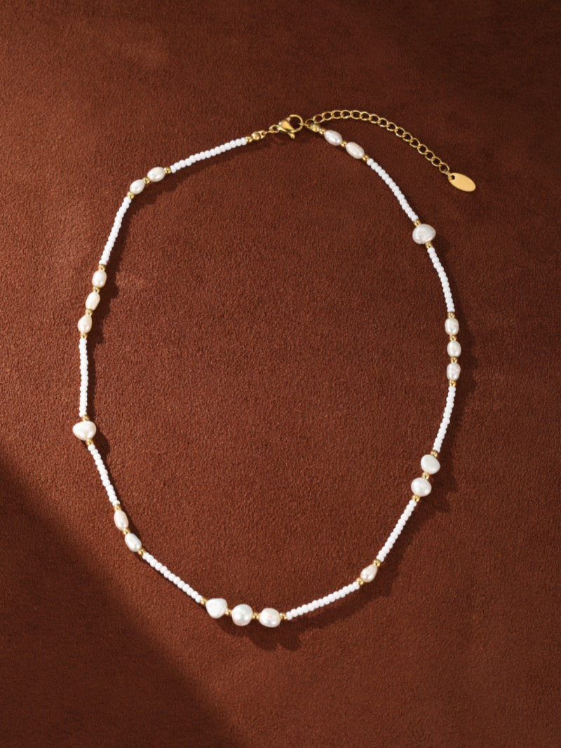 Collier à rang perlé Dune en perle d'eau douce présentant des perles baroques irrégulières entrecoupées de minuscules perles graines blanches et d'accents ton or, avec une chaîne ajustable ton or et un fermoir mousqueton.