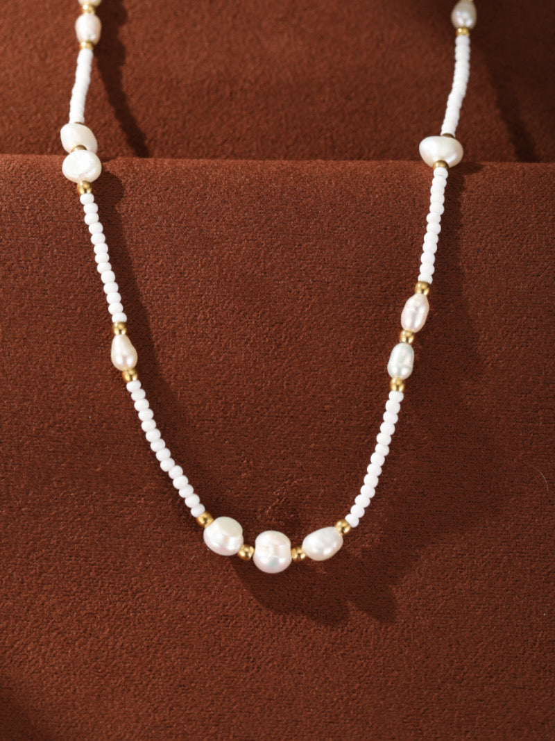 Collier Dune présentant un rang de minuscules perles graines blanches entrecoupées de perles baroques irrégulières d'eau douce et d'accents ton or.