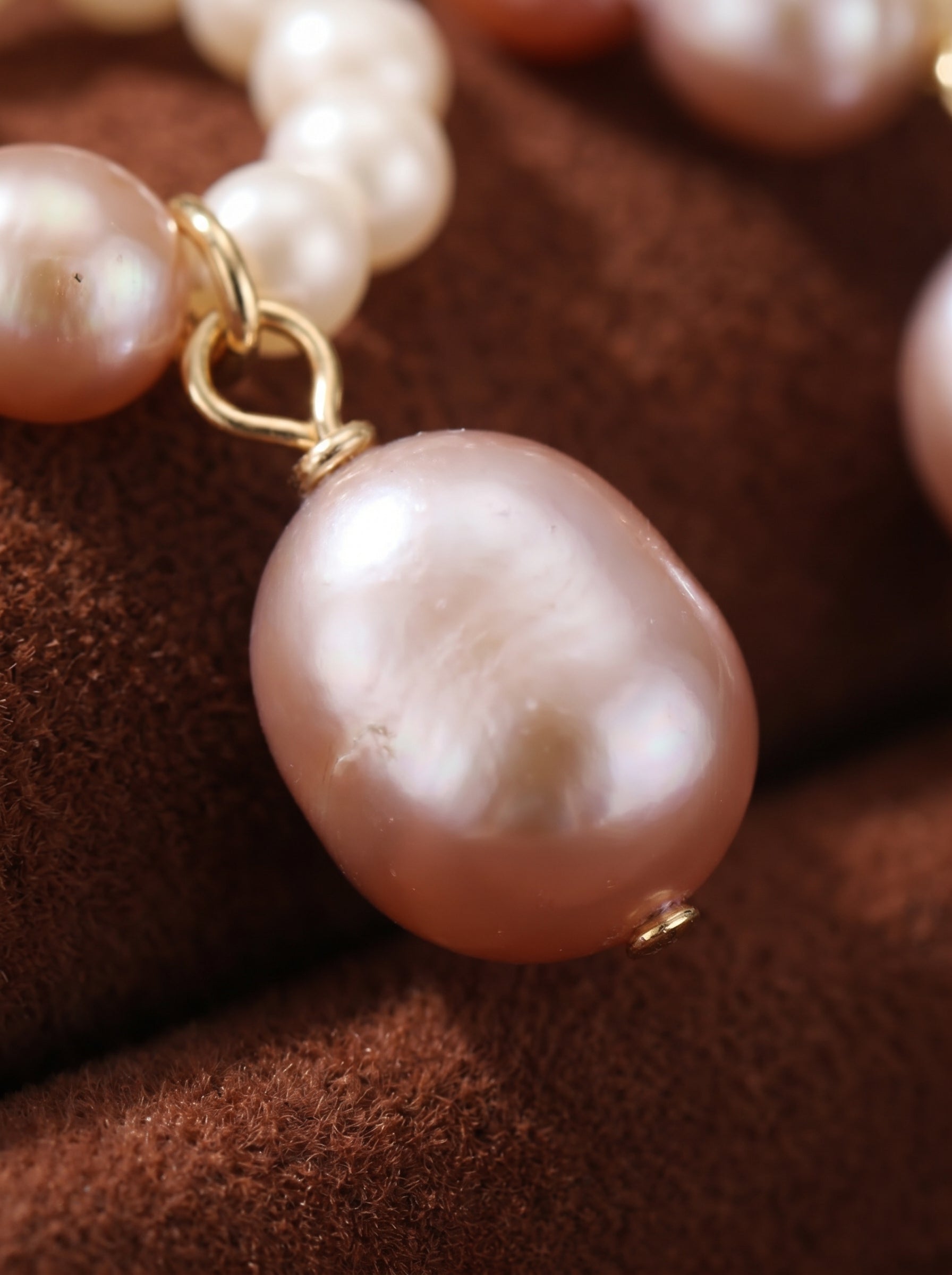 Close-up of Echo Freshwater Pearl Hoop Drop Earrings featuring a large, lustrous pink pearl dangling from a gold hoop adorned with smaller white and pink seed pearls.@pearl